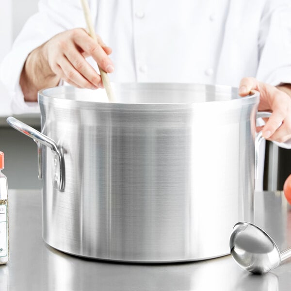 A chef stirring soup in a Vollrath Wear-Ever Classic Select aluminum sauce pot.