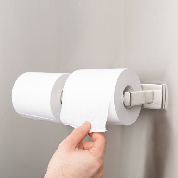 A hand holding a roll of toilet paper on a wall.