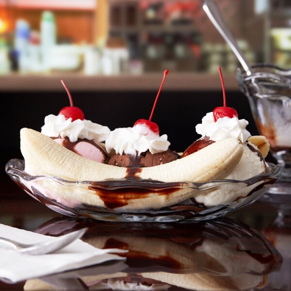 An Anchor Hocking crystal banana split dish filled with a banana split with ice cream, chocolate, whipped cream, and cherries.