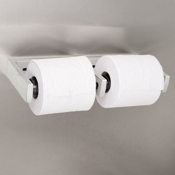 A Bobrick multi roll toilet paper dispenser with one roll of toilet paper.