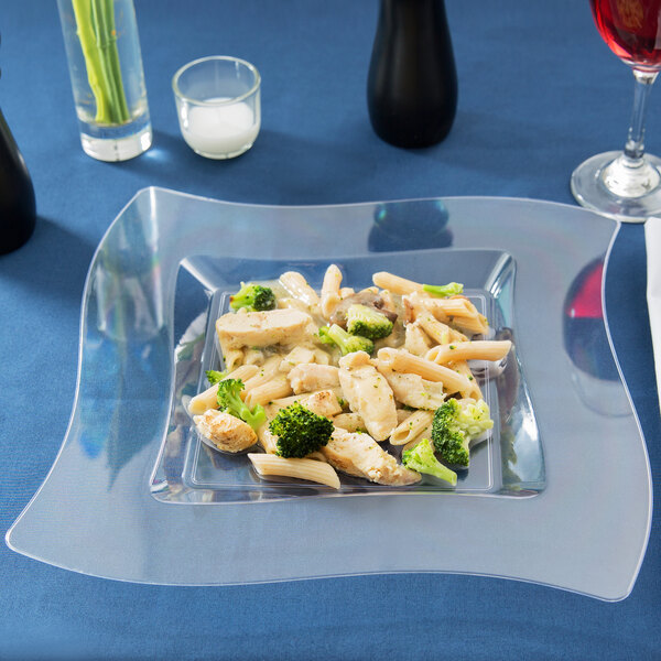 A Fineline clear plastic square plate with pasta and broccoli on a table.