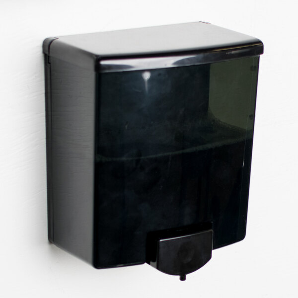 A black Bobrick ClassicSeries surface mounted soap dispenser on a white wall.