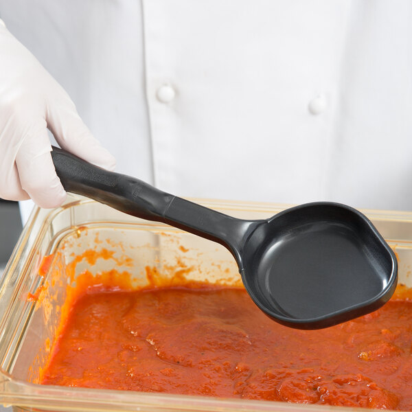 A person in a white glove using a black Vollrath Spoodle to serve red sauce.