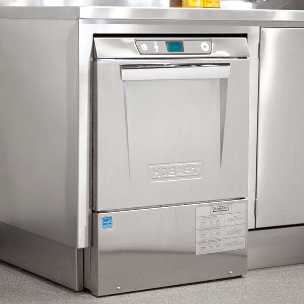 A stainless steel Hobart undercounter dishwasher in a professional kitchen.