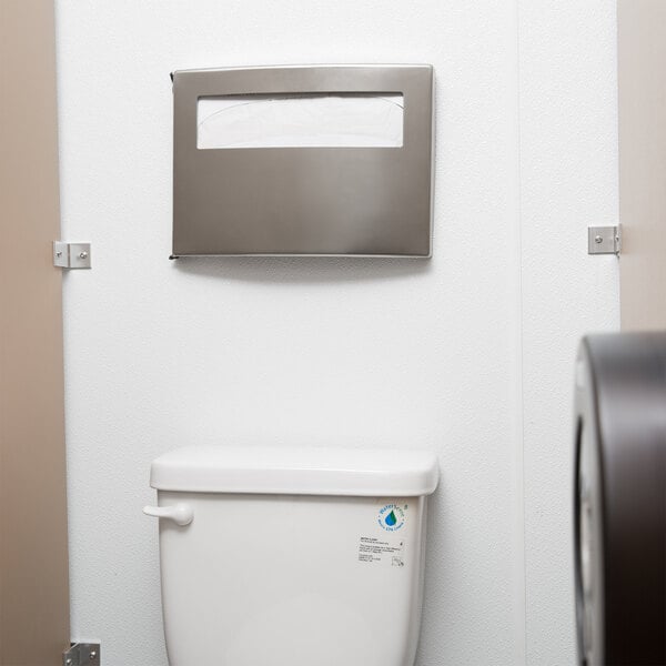 A Bobrick ConturaSeries seat cover dispenser on a wall above a toilet.