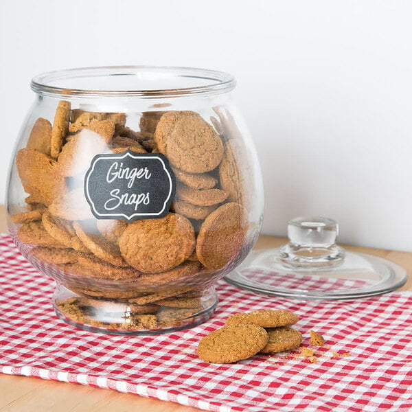 A glass jar of ginger snaps with an American Metalcraft chalkboard label on a table.