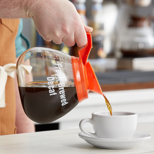 A person pouring decaf coffee from a Grindmaster coffee decanter into a cup.