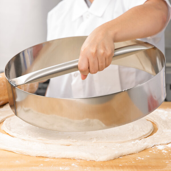 A person using an American Metalcraft stainless steel dough cutting ring to cut dough.