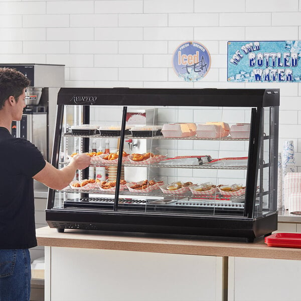 A man standing at a countertop with food in an Avantco heated display case.