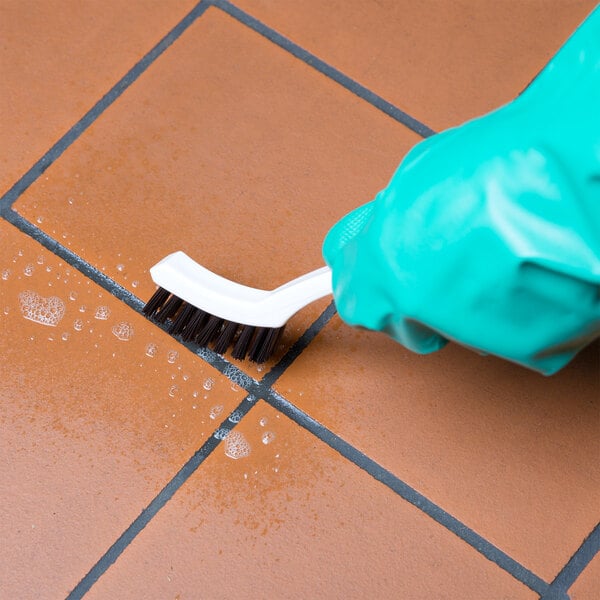 A hand in green glove cleaning tile with a Carlisle Grout Brush.