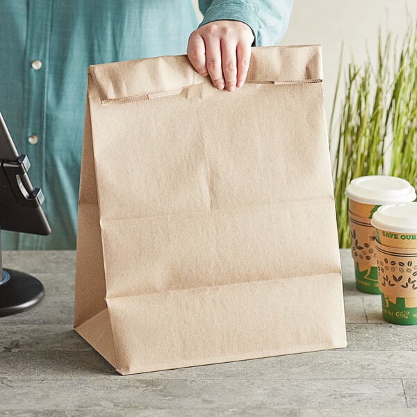 A person holding a Bagcraft brown paper barrel sack bag filled with coffee.