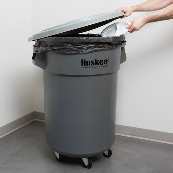 A man using a Continental Huskee 55 gallon gray trash can in a hospital cafeteria.