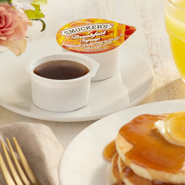 A plate of pancakes with Smucker's Breakfast Syrup and a cup of coffee on a table.