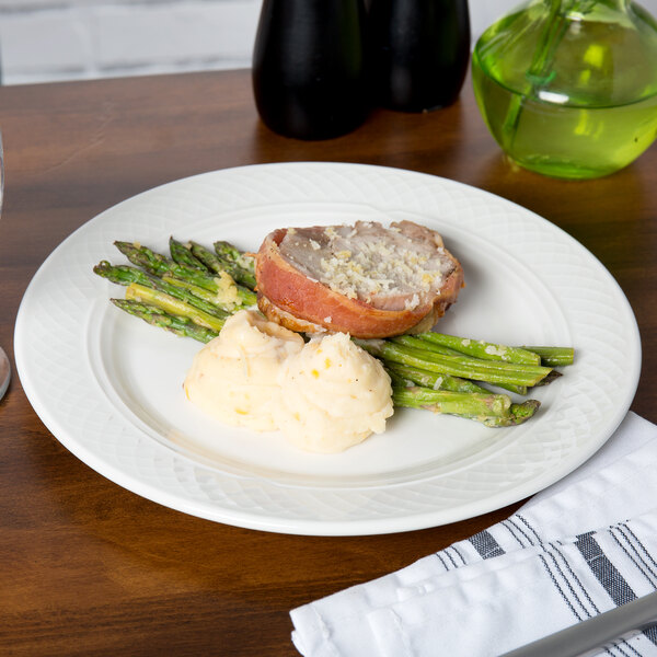 A Homer Laughlin Kensington Ameriwhite bright white china plate with meat, asparagus, and mashed potatoes on a table.