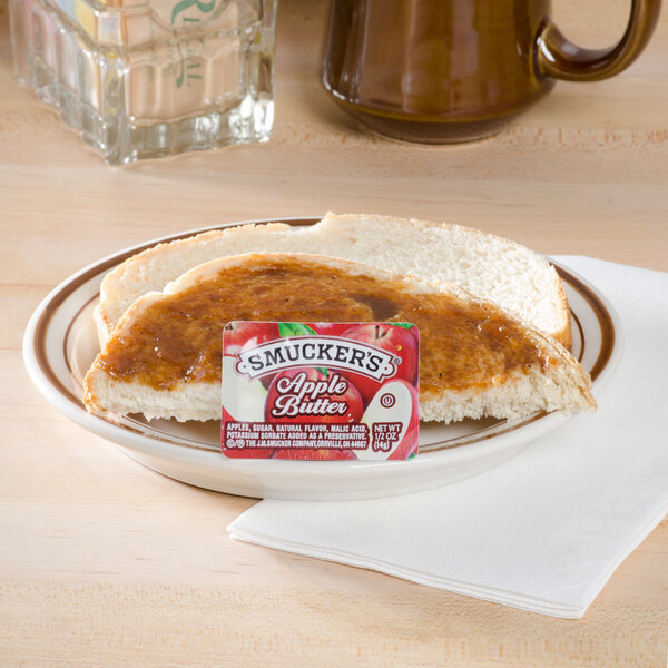 A plate of bread with a Smucker's Apple Butter portion cup spread on it.