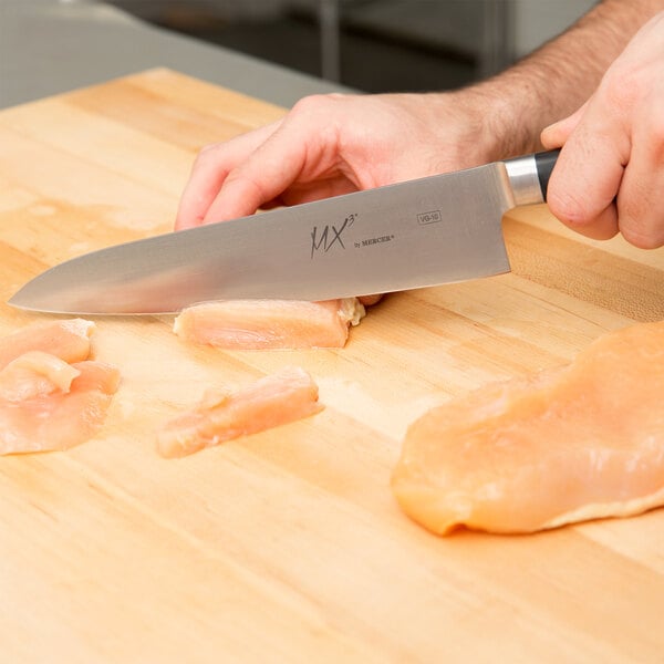 A hand holding a Mercer Culinary MX3 Gyuto knife cutting meat on a wooden surface.