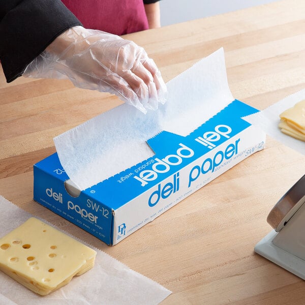 A person in plastic gloves using Durable Packaging deli wrap to cut cheese on a table.
