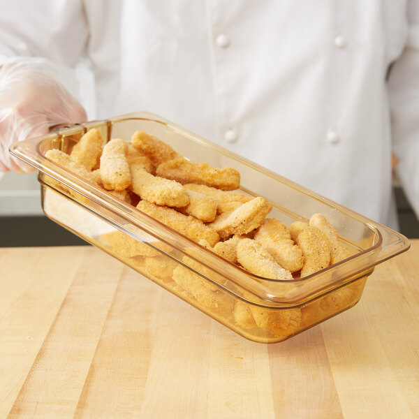 A person holding a Carlisle glass food pan with chicken strips.