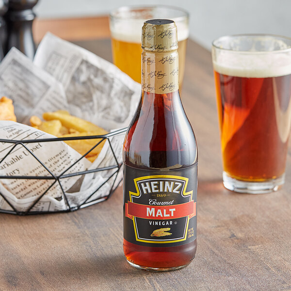 A bottle of Heinz Gourmet Malt Vinegar next to a basket of fries with a glass of beer.