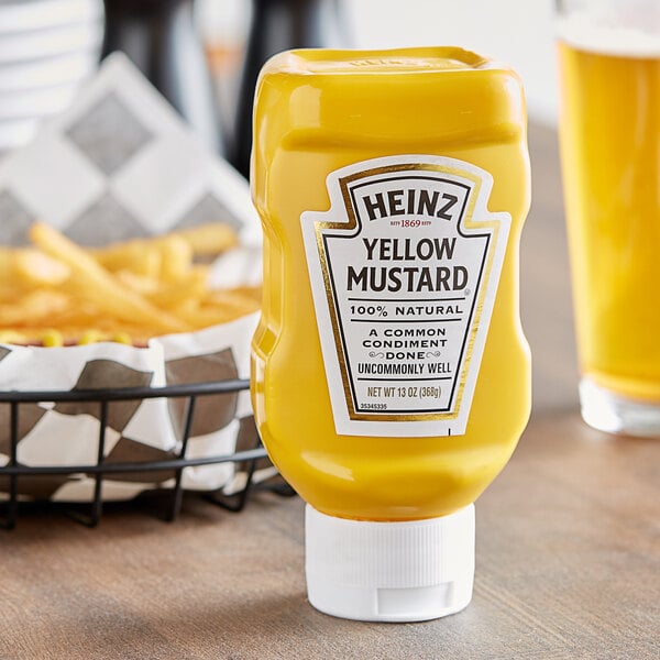 A Heinz yellow mustard squeeze bottle on a table next to a basket of fries.
