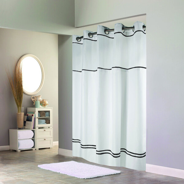 A white Hookless shower curtain with black stripes on a rod in a white bathroom.