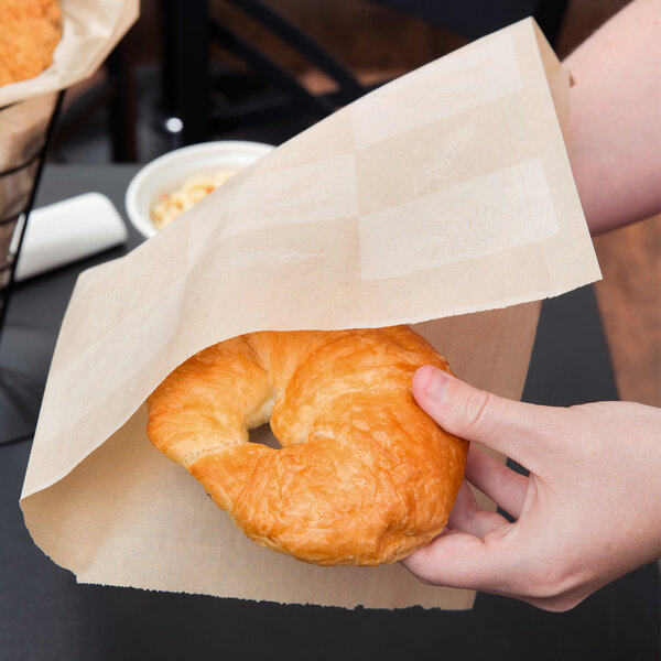 A person holding a Choice natural kraft cone basket liner with croissants inside.