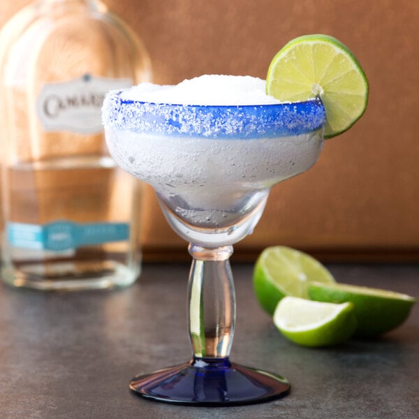 A Libbey margarita glass with a drink, a salted rim, and a lime wedge.