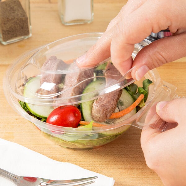 A person holding a Polar Pak clear plastic bowl filled with salad.