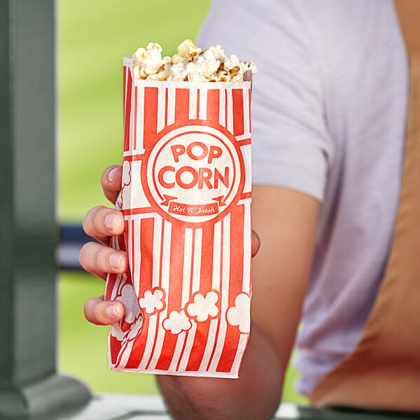 A person holding a red and white striped Carnival King popcorn bag.