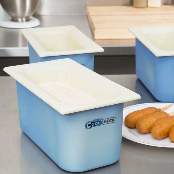 A white Carlisle Coldmaster plastic food pan on a counter in a school kitchen.