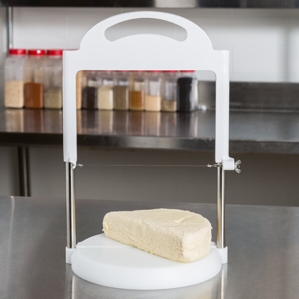 A Matfer Bourgeat cheese slicer on a white counter with a slice of white cheese on it.