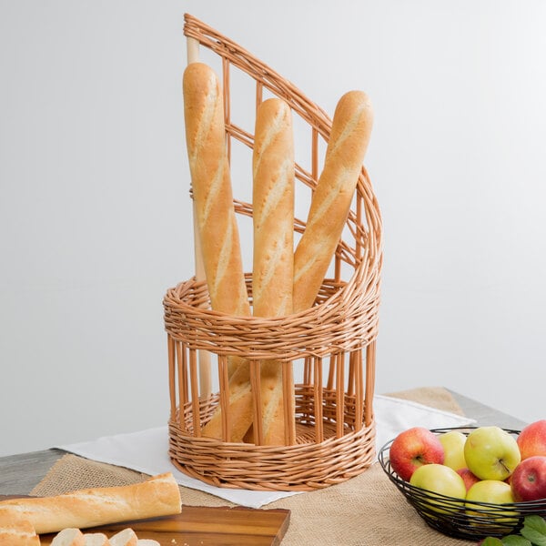 A Matfer Bourgeat round wicker bread basket with bread and fruit on a table in a bakery display.