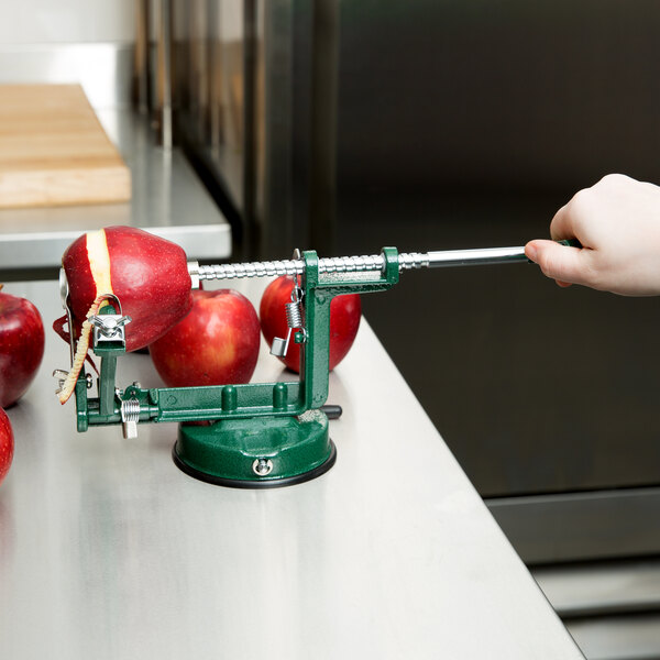 A hand using a green Matfer Bourgeat apple peeler to peel a red apple.
