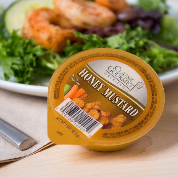 A Classic Gourmet Honey Mustard portion cup on a plate of shrimp.