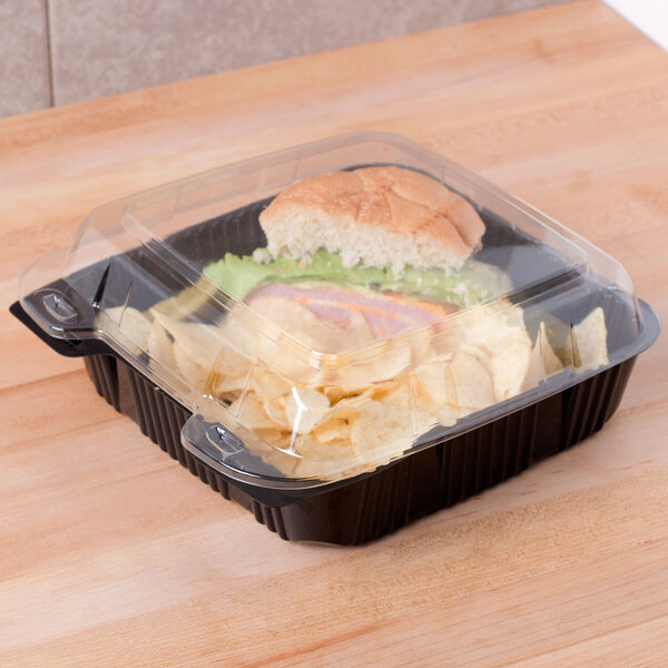 A Polar Pak plastic container with a sandwich and chips on a wooden surface.