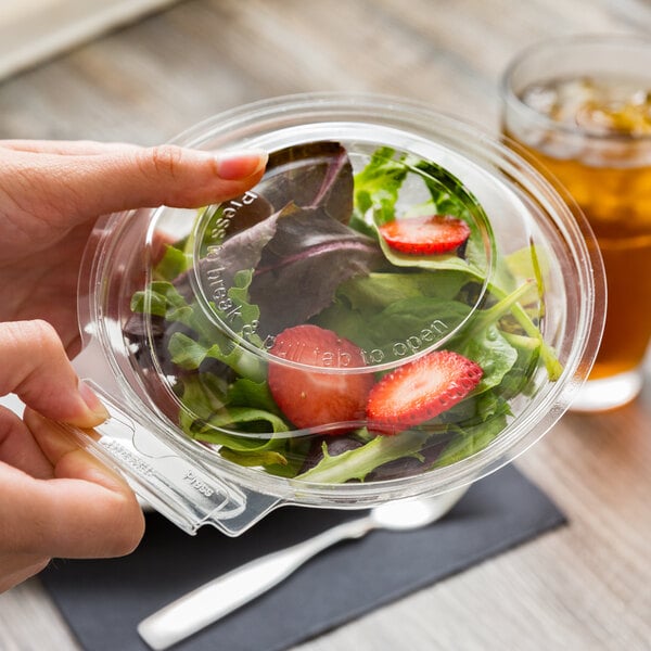 A hand holding a Polar Pak clear plastic container of salad with a red lid.