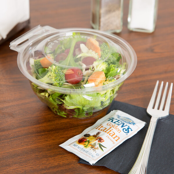 A Polar Pak clear plastic bowl of salad with a fork and spoon on a table.