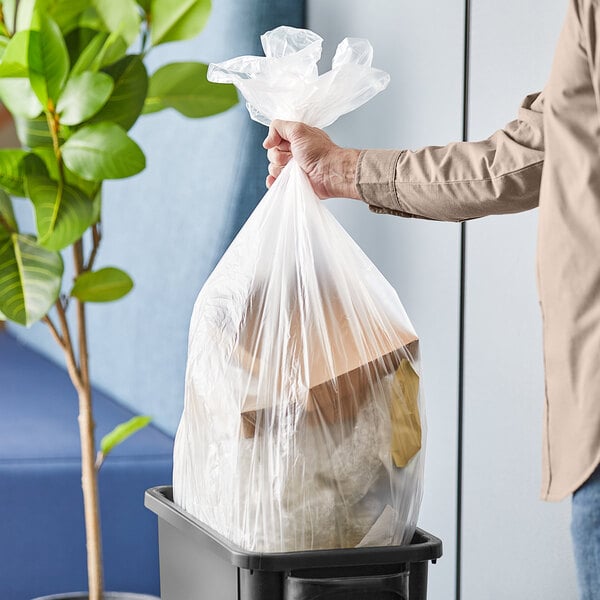 A person holding a Lavex plastic bag full of trash in a trash can.