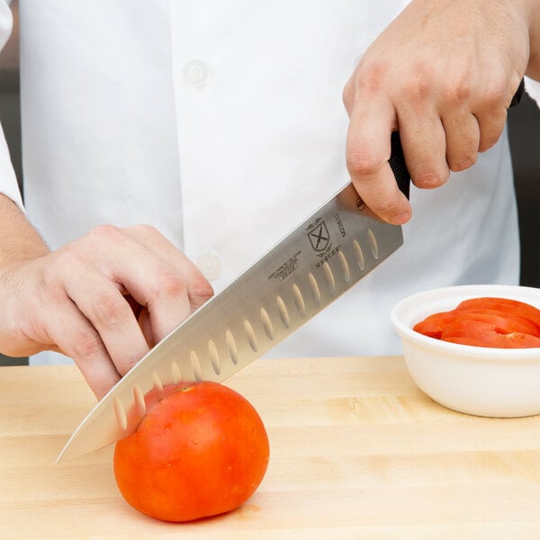 A person cutting a tomato with a Mercer Culinary Millennia Chef Knife.