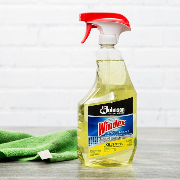 A spray bottle of yellow SC Johnson Windex on a table with a green cloth on top.