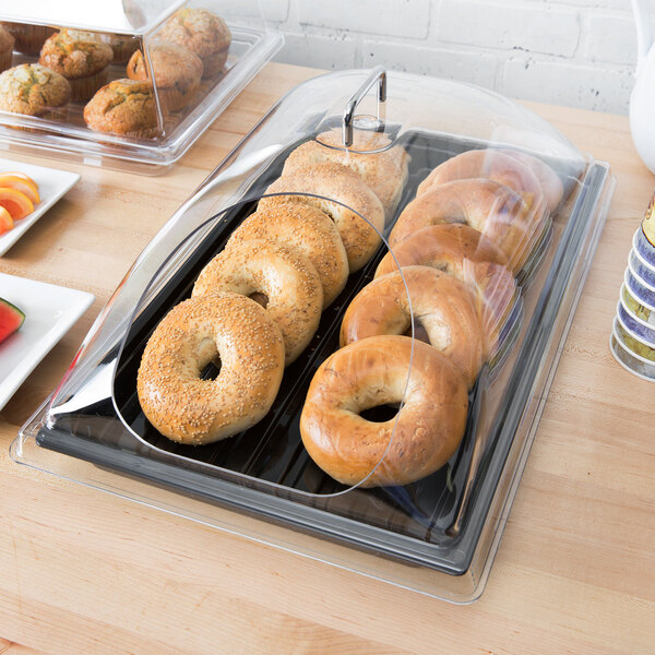 A black polycarbonate display tray with bagels, muffins, and croissants on it.
