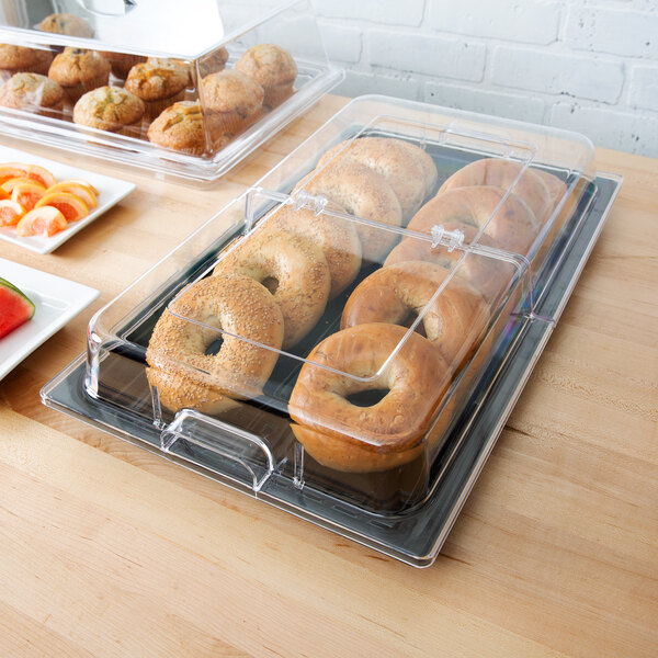 A black polycarbonate tray with bagels and fruit with a clear plastic lid.