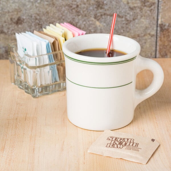 A Homer Laughlin green banded mug of coffee on a table with a packet of sugar.