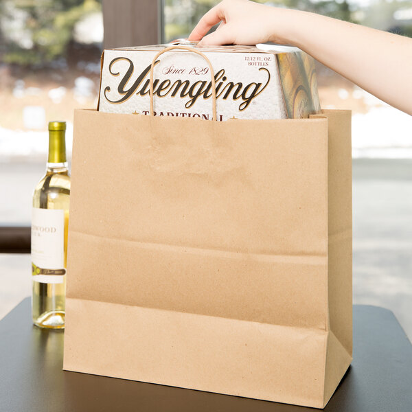 A person holding a Duro Jr. Mart brown paper shopping bag with a box of bottles in it.