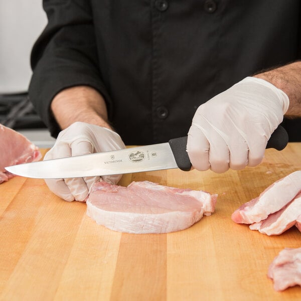 A person in gloves using a Victorinox Flank and Shoulder Knife to cut meat on a cutting board.