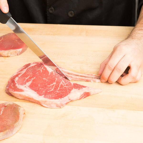 A person using a Victorinox Stiff Flank and Shoulder Knife to cut meat on a cutting board.