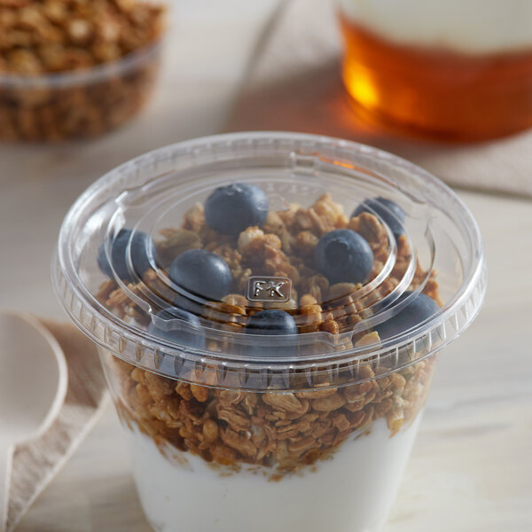 A Fabri-Kal clear plastic flat lid on a cup of yogurt with granola and blueberries.