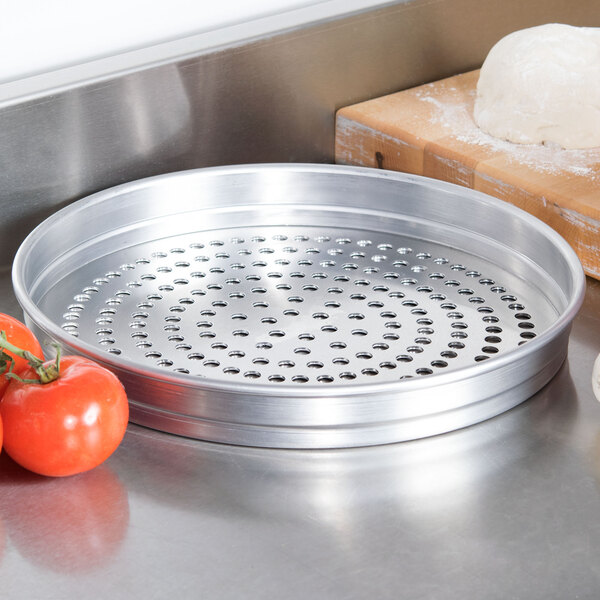 An American Metalcraft Super Perforated Pizza Pan with tomatoes and dough on a wooden surface.