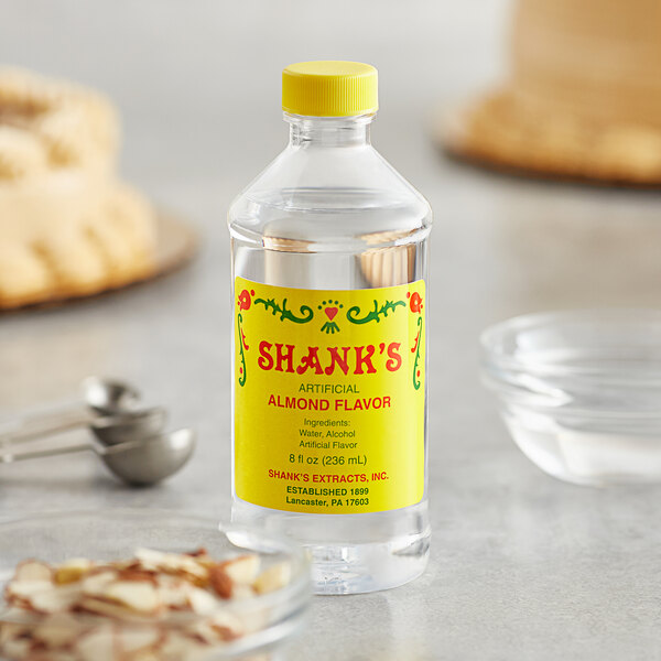 A bottle of Shank's Imitation Almond Flavoring on a table next to a bowl of sugar.