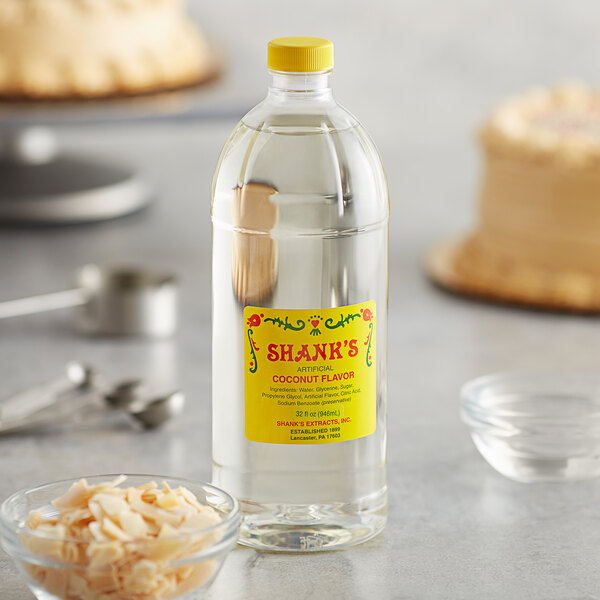A bottle of Shank's Imitation Coconut Extract on a counter next to a bowl of coconut shavings.